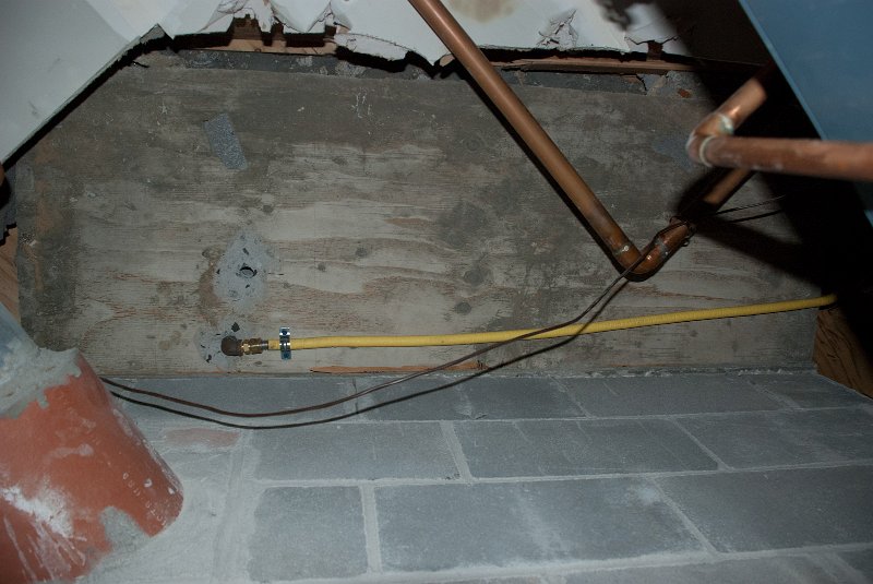 DSC_9162.jpg - The gas supply (yellow flex) is brougt in beneath the fireplace.  This view is looking up at the concrete slab base of the fireplace.  I used my larger rotary hammer to bore through the slab.